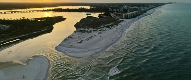 Aerial view of a Florida inlet at golden sunset with white sand beach, waterway, and bridge in the distance