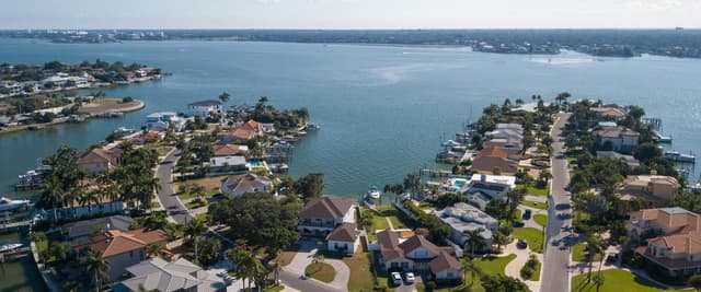Aerial view of a Florida coastal neighborhood with waterways, palm trees, and tiled rooftops under a clear blue sky