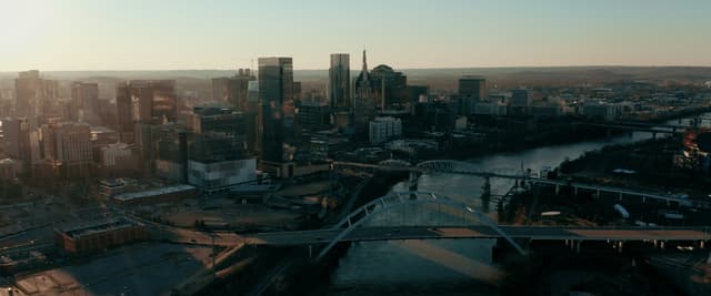 Aerial view of downtown Nashville at dusk with the Cumberland River, bridges, and city skyline lit by fading golden light