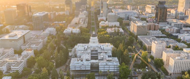 Aerial view of Sacramento at sunrise with the California State Capitol dome surrounded by tree-lined streets and city buildings bathed in golden light