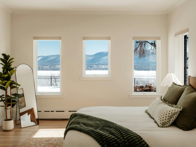 Airy private bedroom with cream walls, three windows with mountain views, green throw, and fiddle-leaf fig plant