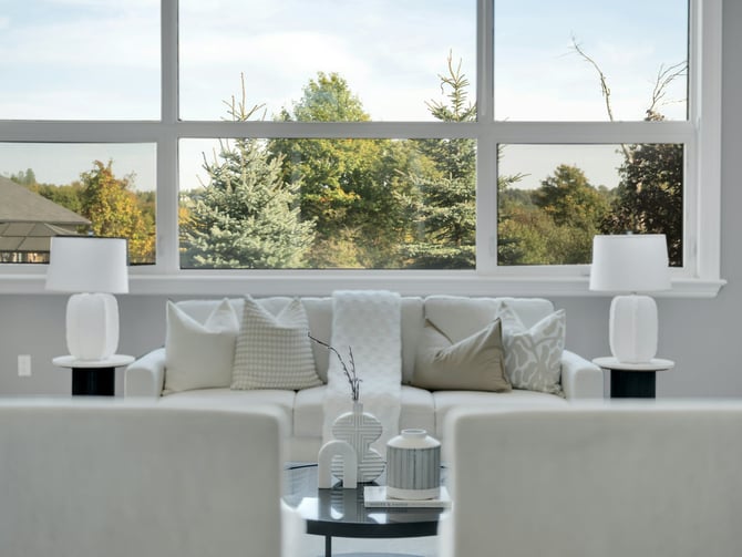 Bright white shared living room with large picture window overlooking autumn trees, white sofa and matching armchairs